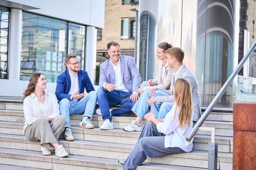 Das Team der open next GmbH im Rhienauhafen. Menschen sitzen auf einer Treppe und lachen.